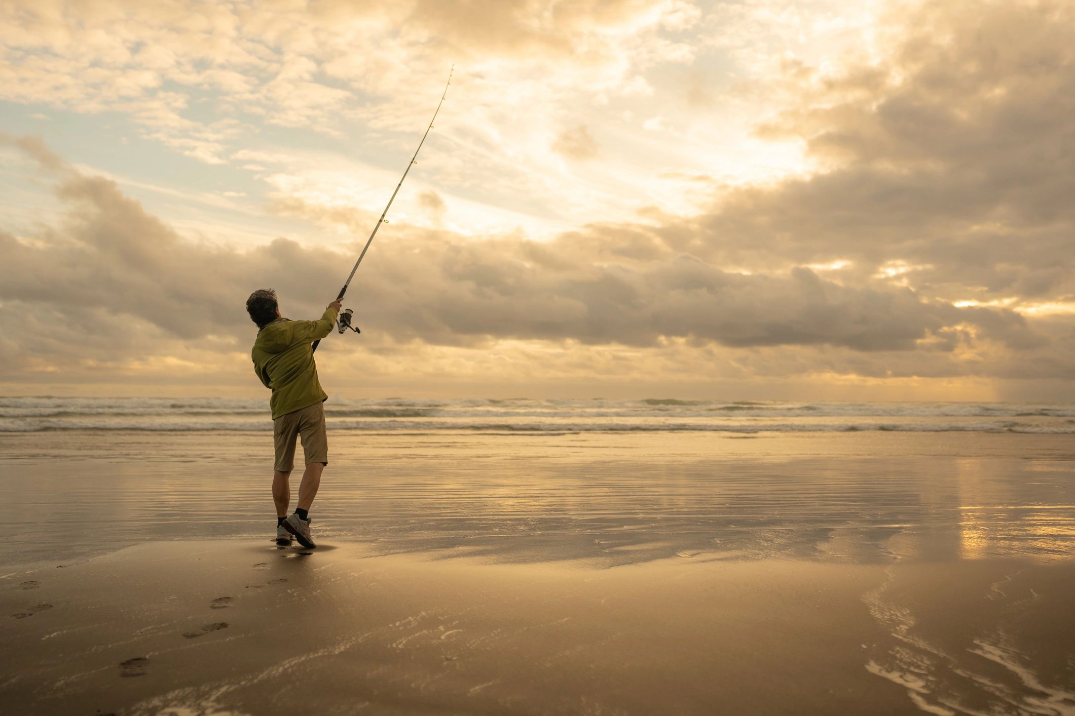 Angler surf casting at sunset